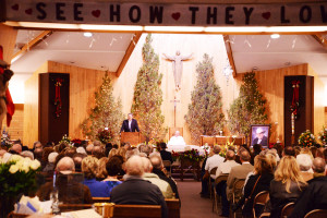 Ty Thompson, at left, speaks at Pat Goggins' funeral Wednesday morning as Rev. Dave Reichling listens. More than 800 people attended the Mass at St. Bernard's Catholic Church. (Judy Killen photo) 