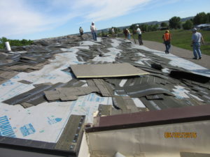 Shingles torn off the existing Huntley Project High School roof lie in the foreground as workers look over another part of the roof on June 3. (photo courtesy of Dane Bradford/HP Schools)
